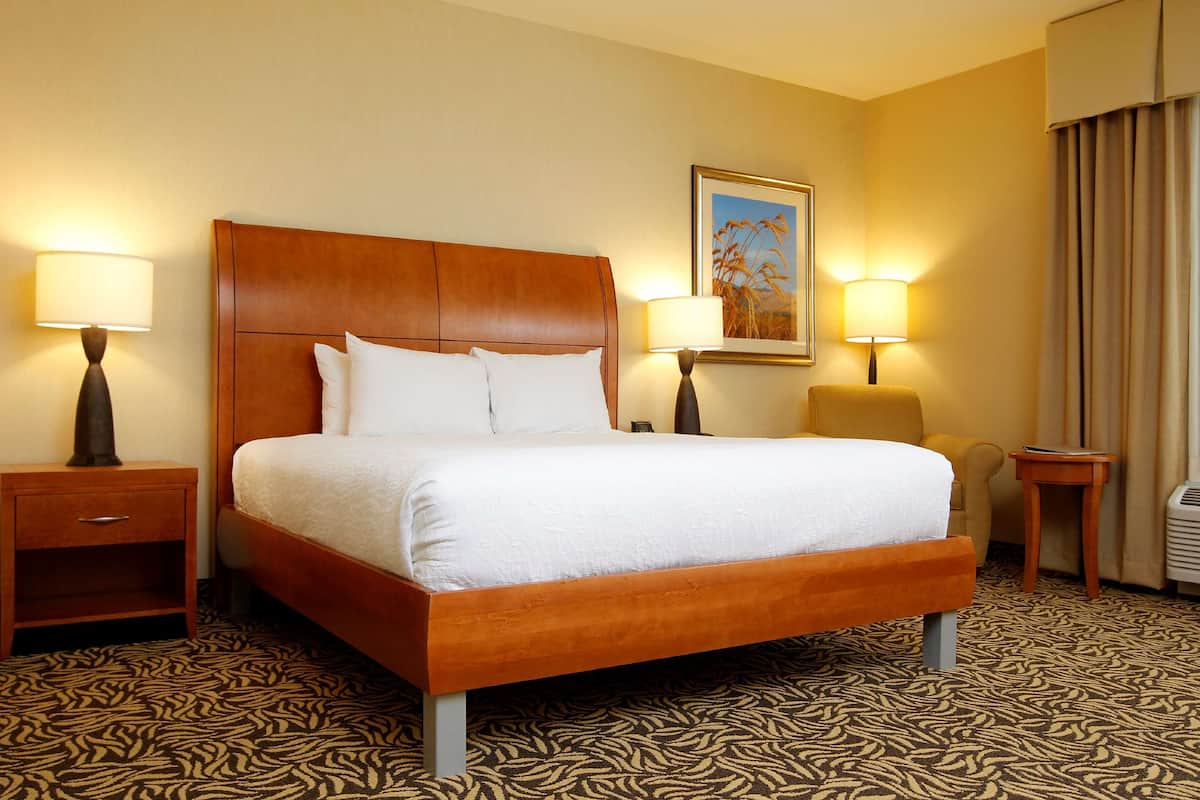 A hotel room with a large bed, two bedside tables with lamps, a chair, and a patterned carpet.