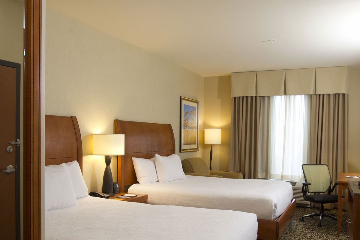 A hotel room with two beds, a desk, a chair, and a window with curtains.