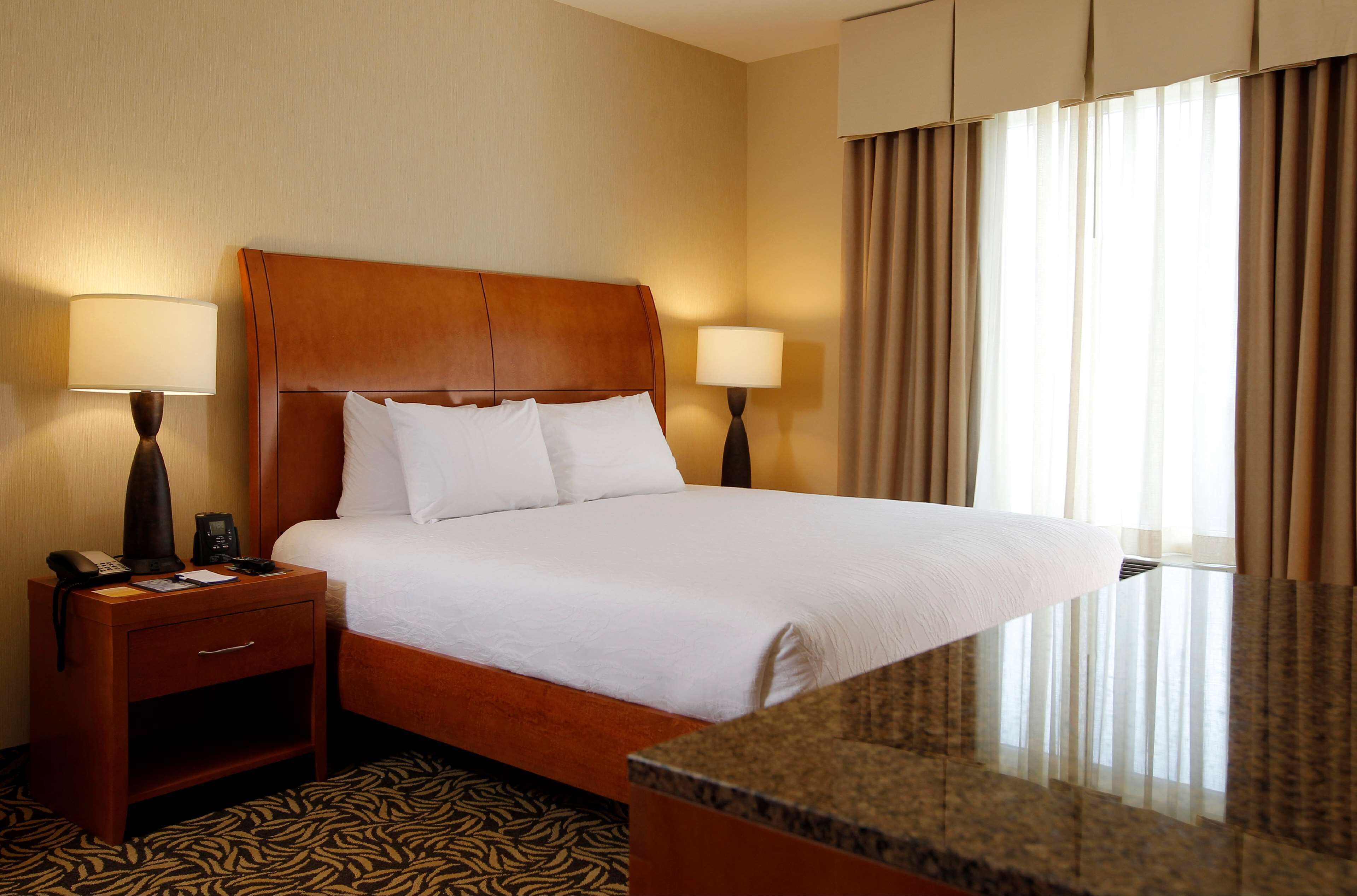 A hotel room with a large bed, two bedside tables with lamps, a wooden headboard, and a patterned carpet.