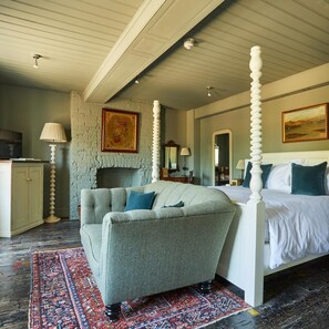 Een slaapkamer met een hemelbed, een bank, een open haard en een groot vloerkleed.