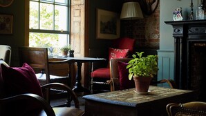 Una habitación con una mesa de madera, sillas, una planta en maceta, una silla roja, una lámpara y una chimenea.