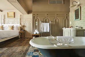 Een slaapkamer met een groot bad, een bed, een nachtkastje en een spiegel.