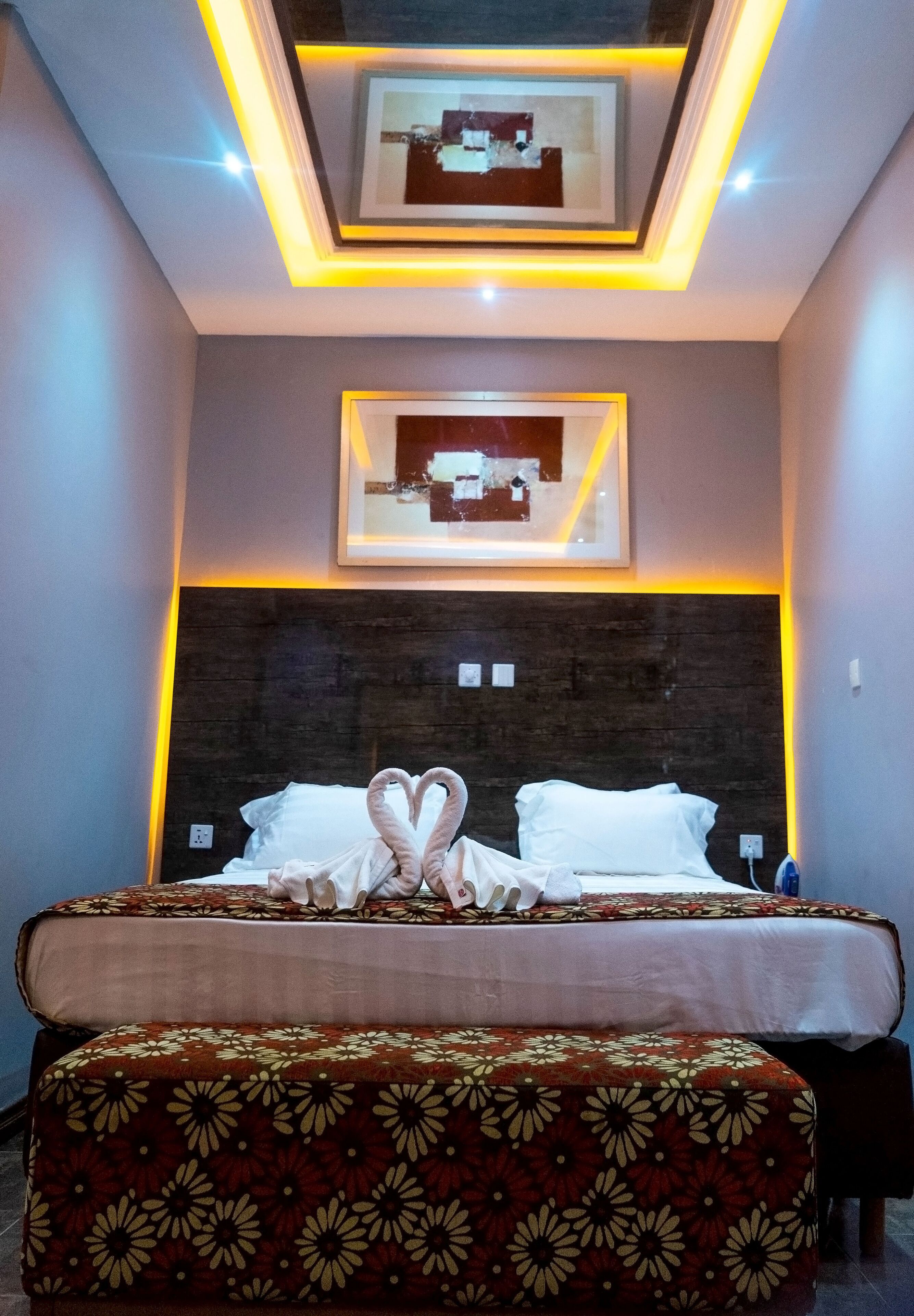 Habitación de hotel con una cama grande, cabecera con acabado de madera oscura, mesita de noche y un cuadro enmarcado sobre la cama.