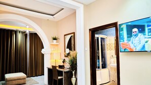 A hotel room with a bed, a desk, a chair, a TV, and a bathroom visible through an open door. - Grand Casamora (Accra)