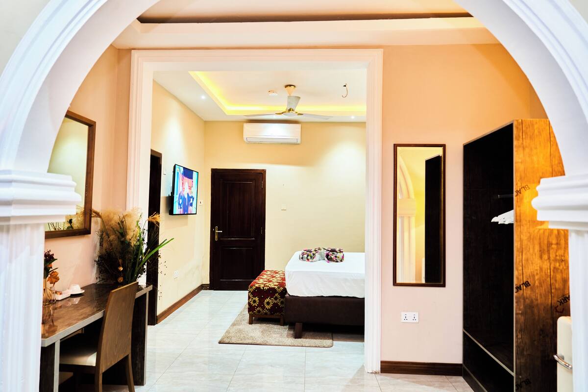 A hotel room with a bed, a desk, and a chair. There is a door leading to another room.