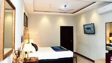 A hotel room with a bed, bedside table, lamp, mirror, TV, and an air conditioning unit.