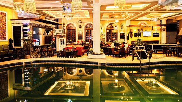 A hotel lobby with a central pool, seating areas, and a bar. - Grand Casamora (Accra)