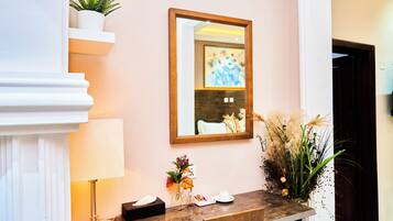 A reception desk with a mirror, a vase with flowers, a lamp, and a small plant on a shelf.