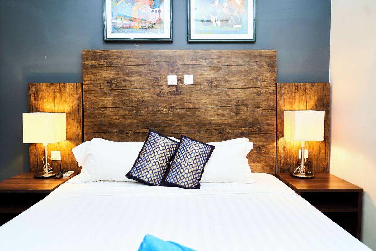 A hotel room with a wooden headboard, white bedding, two lamps on nightstands, and two framed pictures on the wall.