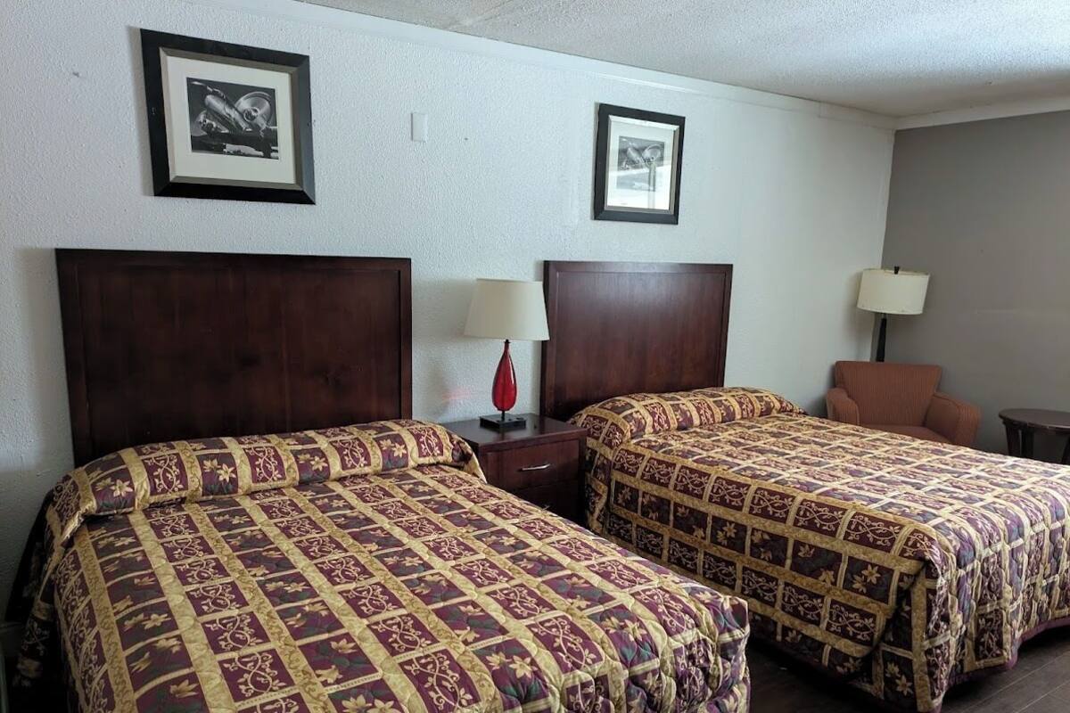 A hotel room with two beds, a nightstand, a lamp, and two framed pictures on the wall.