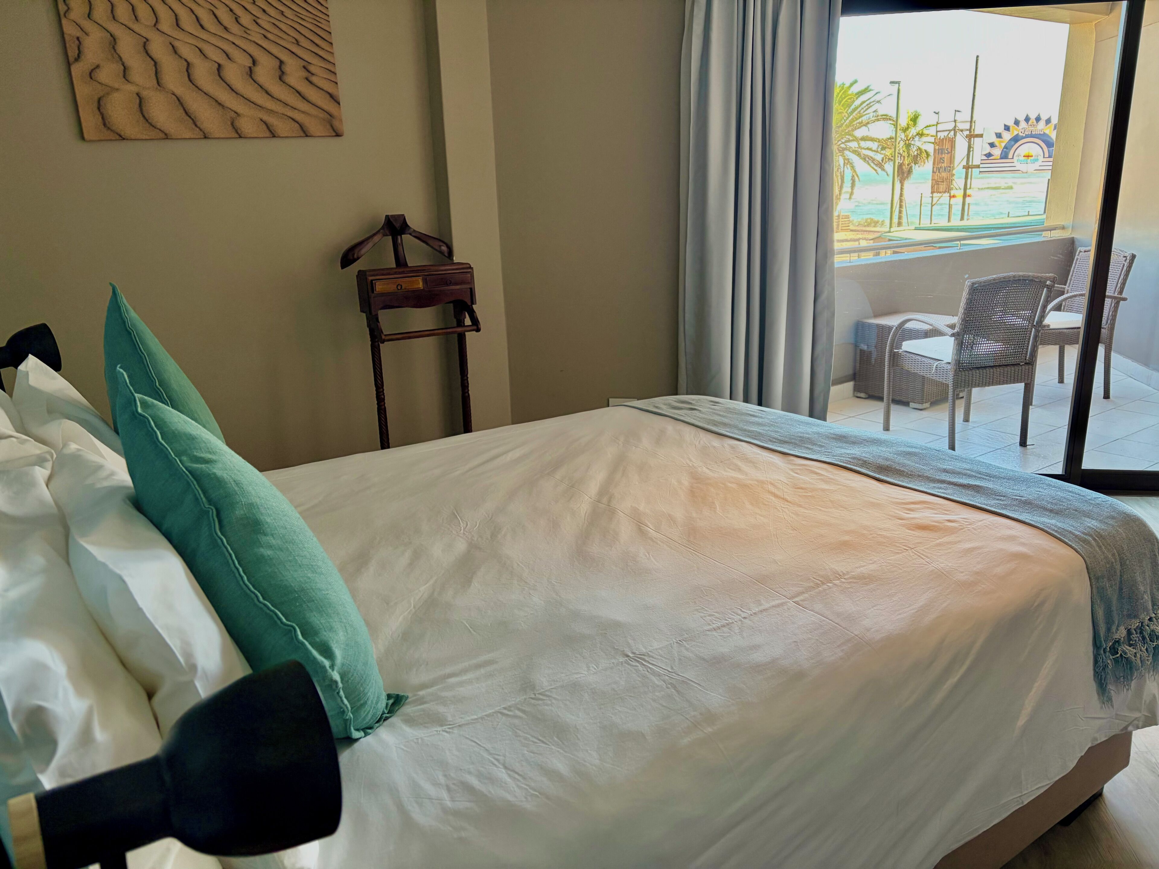 Habitación de hotel con cama, perchero y vistas a un balcón con mobiliario exterior.