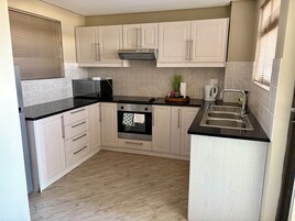 Una cocina con armarios de tonos claros, encimera negra, horno empotrado y un lavabo.