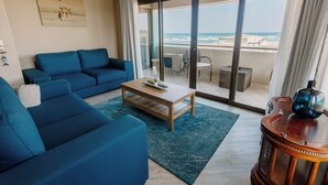 Un saló modern amb un sofà blau, una taula de centre de fusta i vista a l'oceà a través de grans portes de vidre.