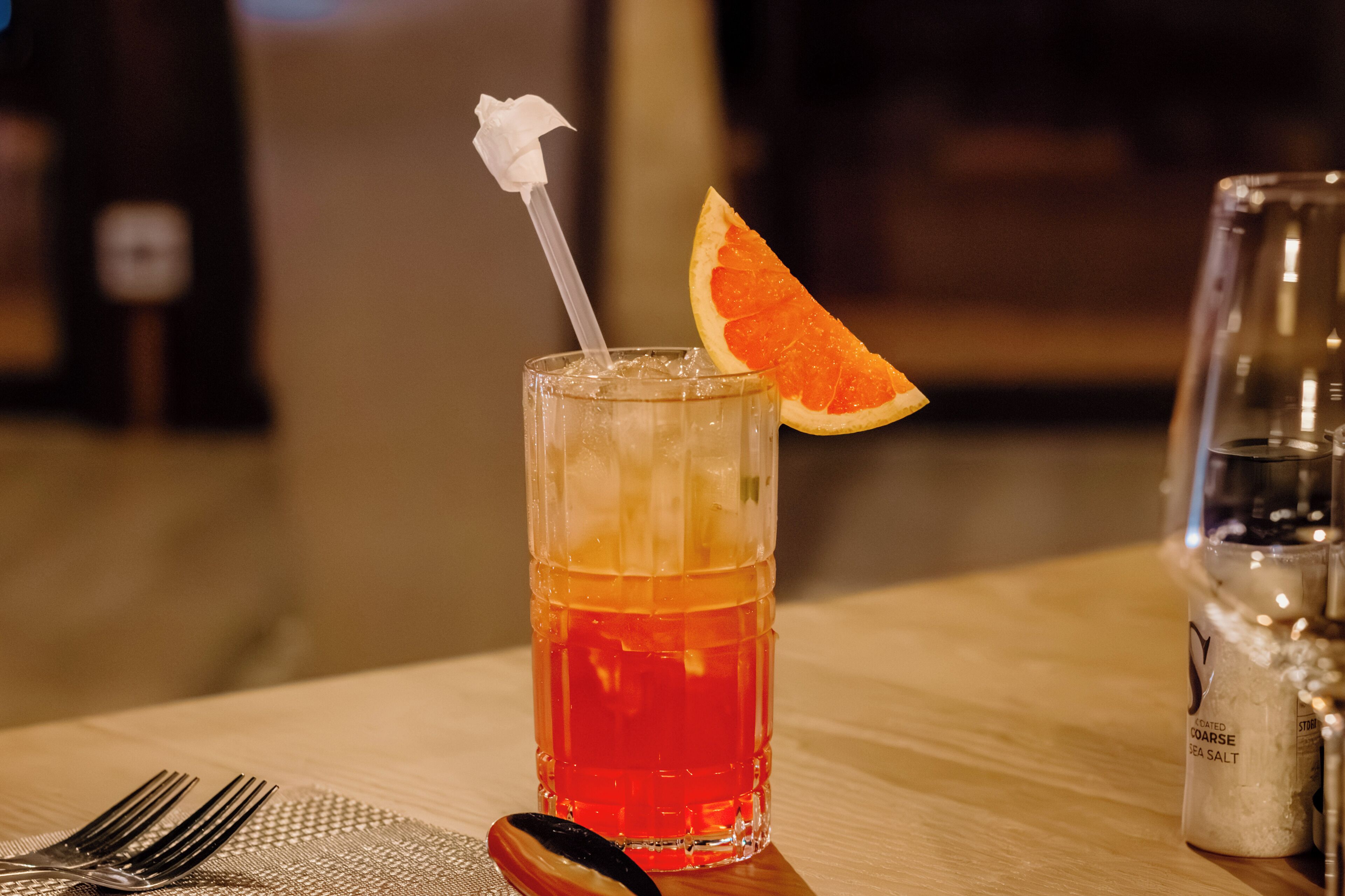 Un vaso de bebida roja con una rodaja de naranja y una flor blanca sobre una mesa.