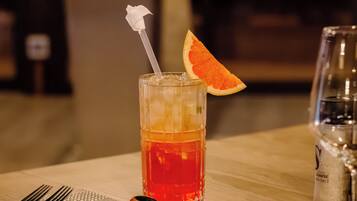 Un vaso de bebida roja con una rodaja de naranja y una flor blanca sobre una mesa.