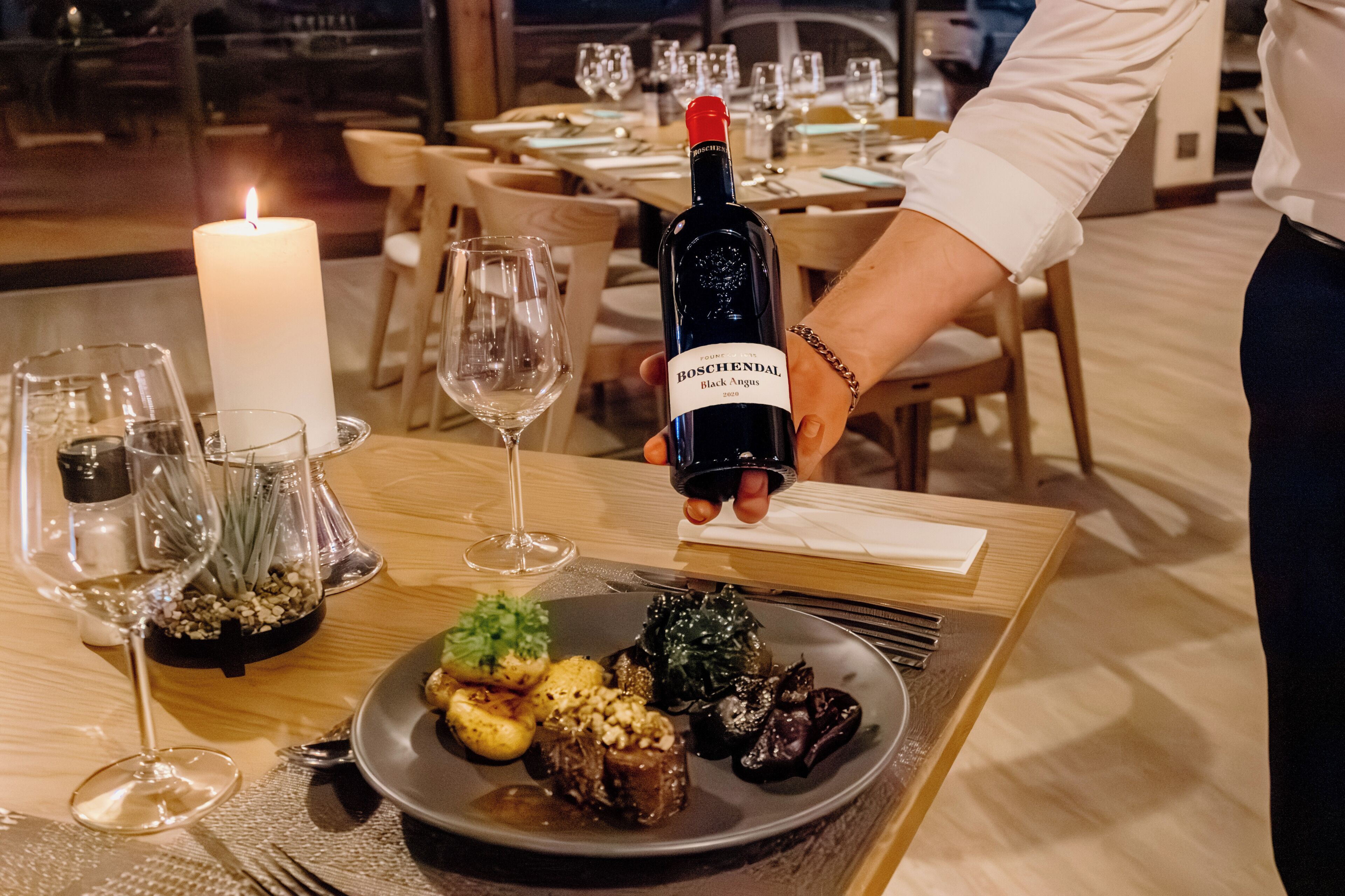 A dining table with a candle, wine glasses, and a plate of food.