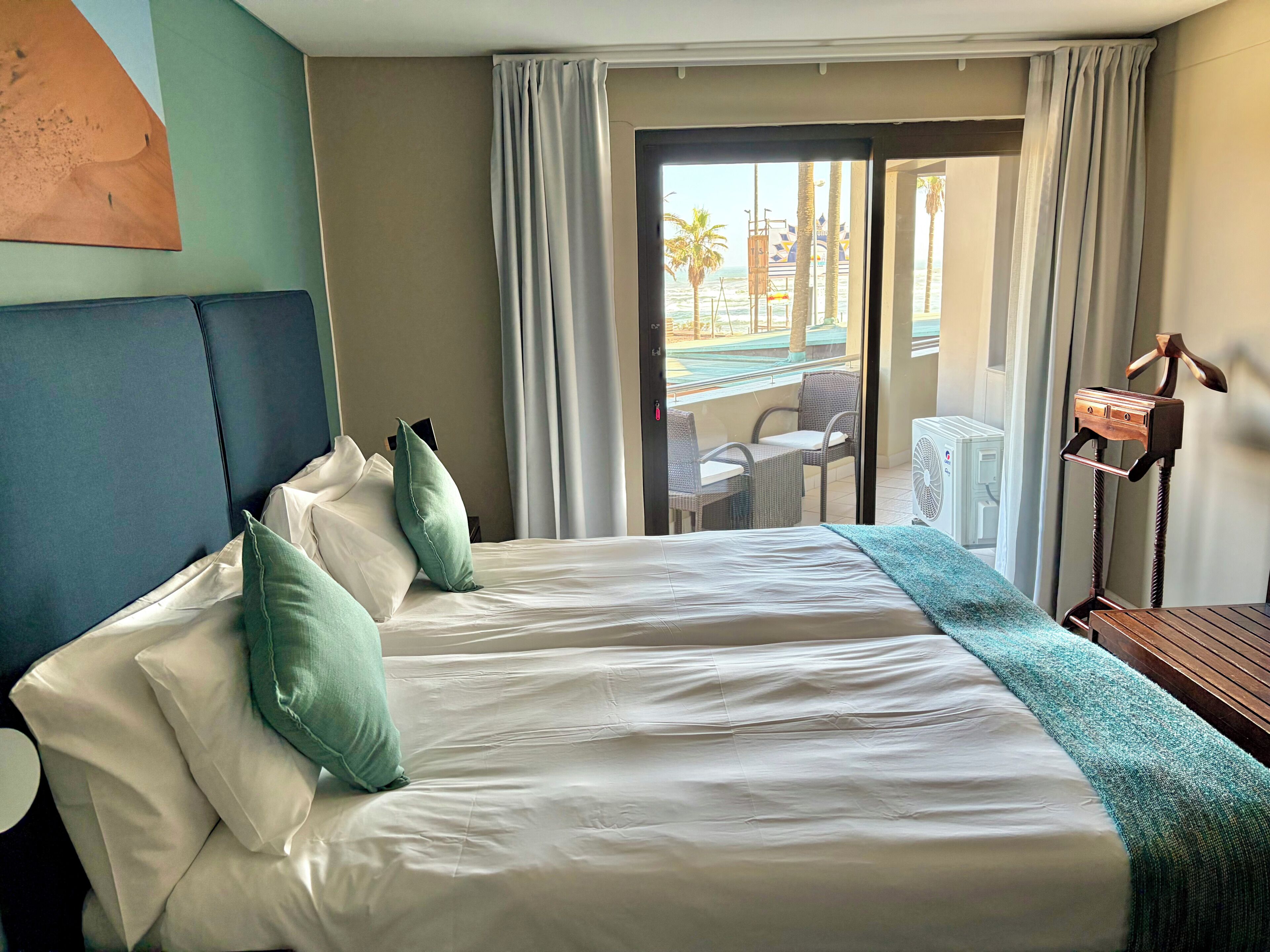 Ein Hotelzimmer mit Bett, Kissen, Schreibtisch und Blick auf den Strand.
