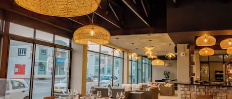 Restaurante moderno com janelas amplas, iluminação pendente em vime e um espaço de bar.