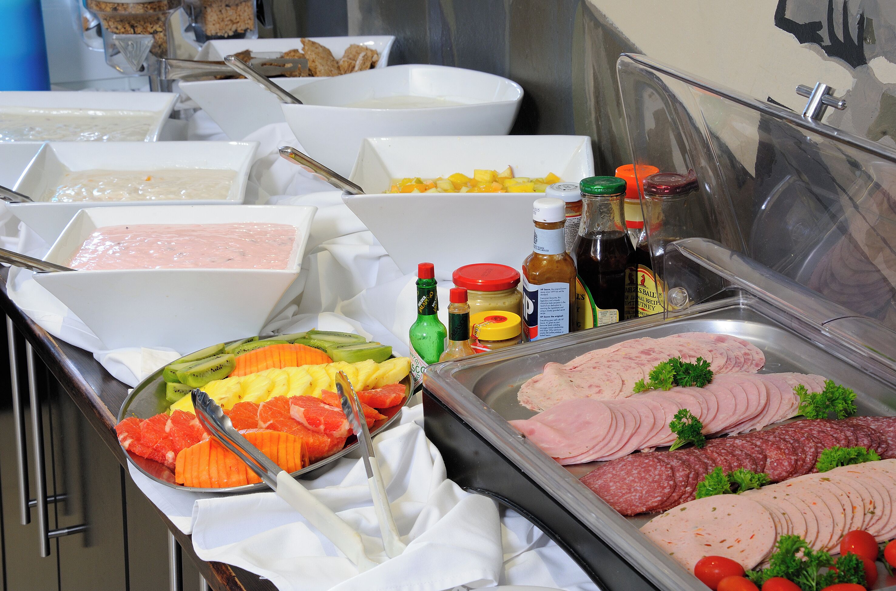 Een buffet met diverse gerechtjes, waaronder fruit, vleeswaren en sauzen.