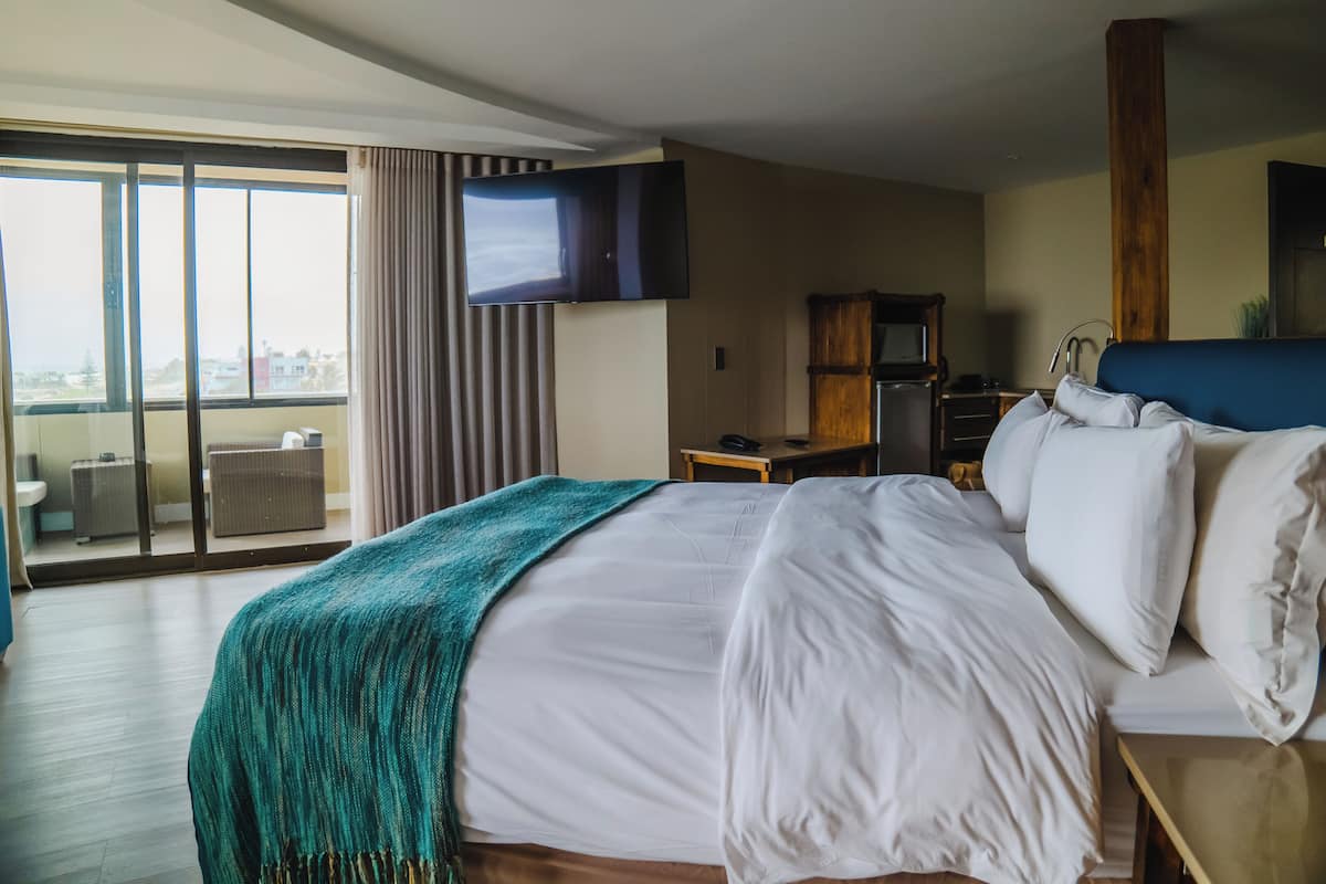 A hotel room with a large bed, a television, a desk, and a view of the city.