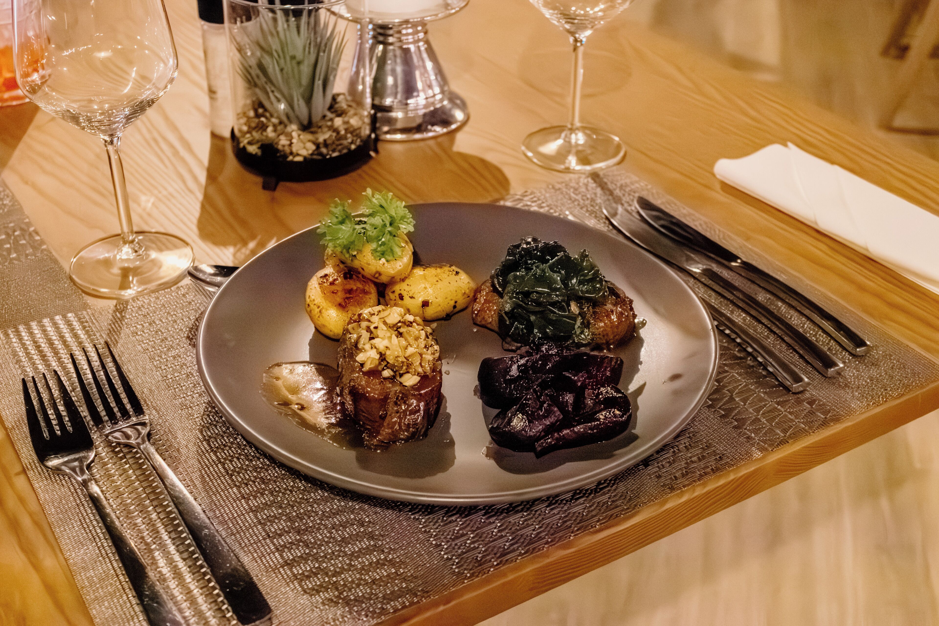 Una mesa de comedor con un plato de comida, cubiertos y vasos.