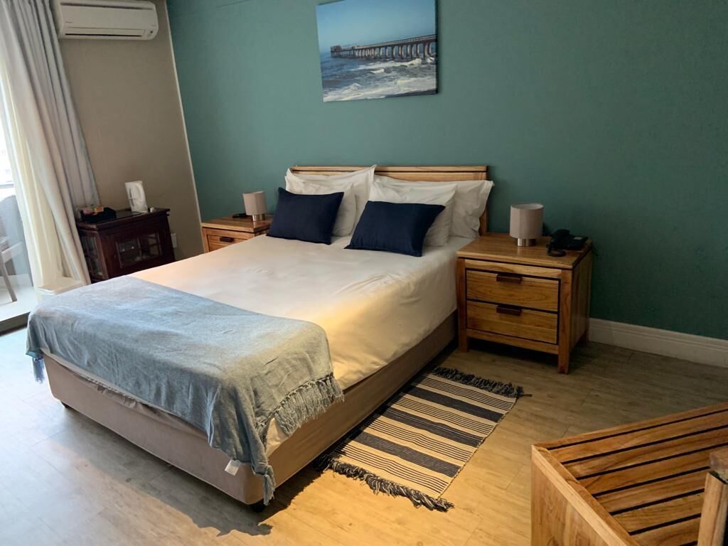 A bedroom with a bed, nightstands, a bedside table, a window with curtains, and a painting on the wall.