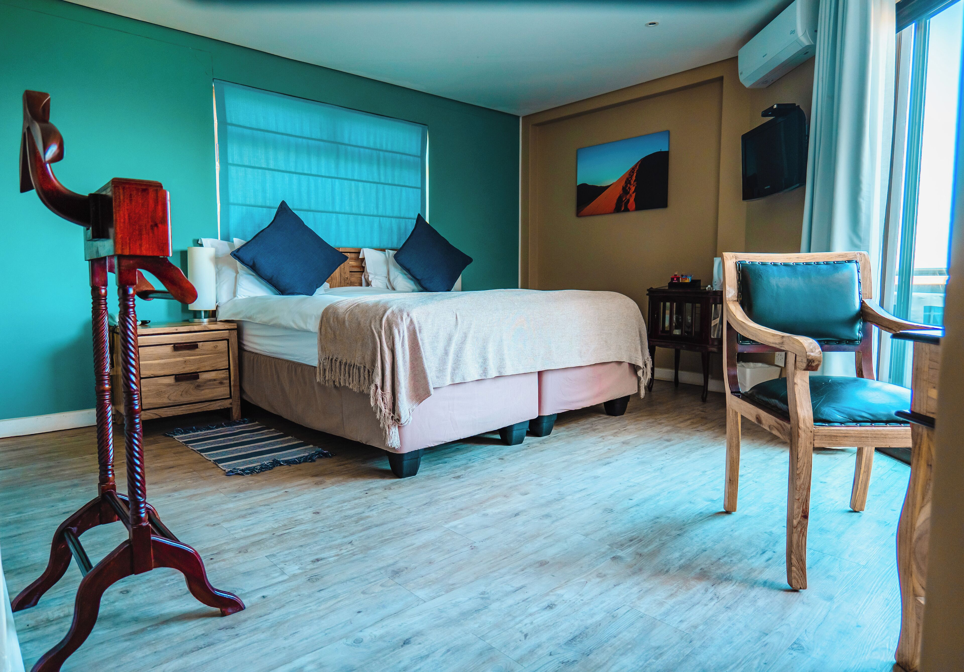 A bedroom with a bed, bedside table, chair, and artwork on the wall.