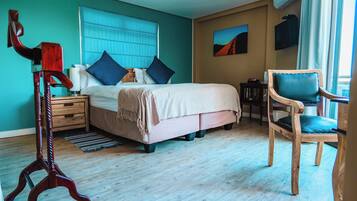 A bedroom with a bed, bedside table, chair, and artwork on the wall.