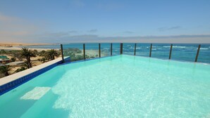 Una piscina d'aigua turquesa, de forma allargada, amb vistes a l'oceà i a la platja.