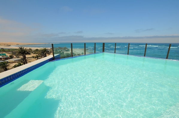 A clear blue infinity pool with a view of the ocean and beach.