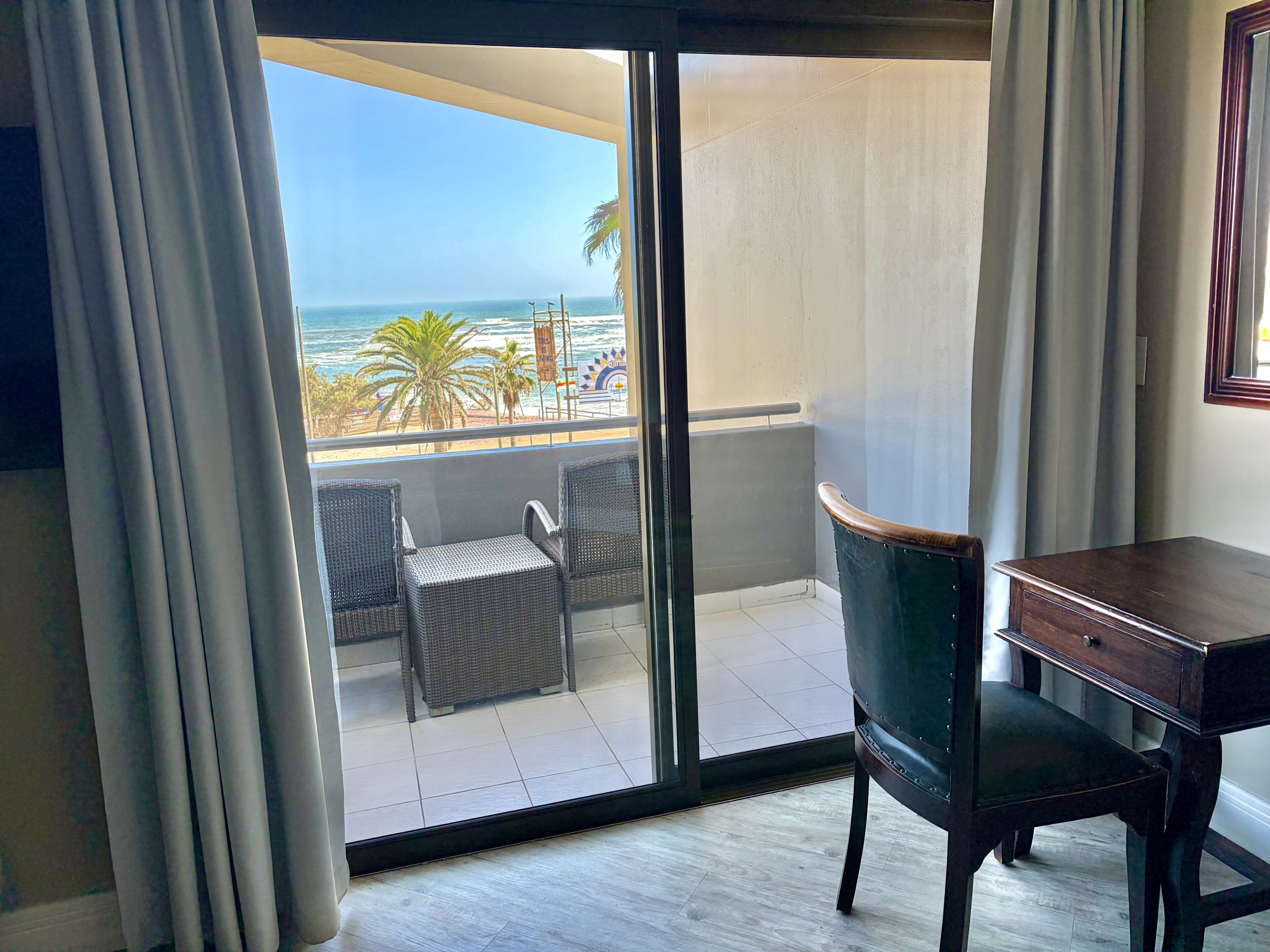 A room with a view of the ocean, a desk, a chair, and a balcony with wicker furniture.