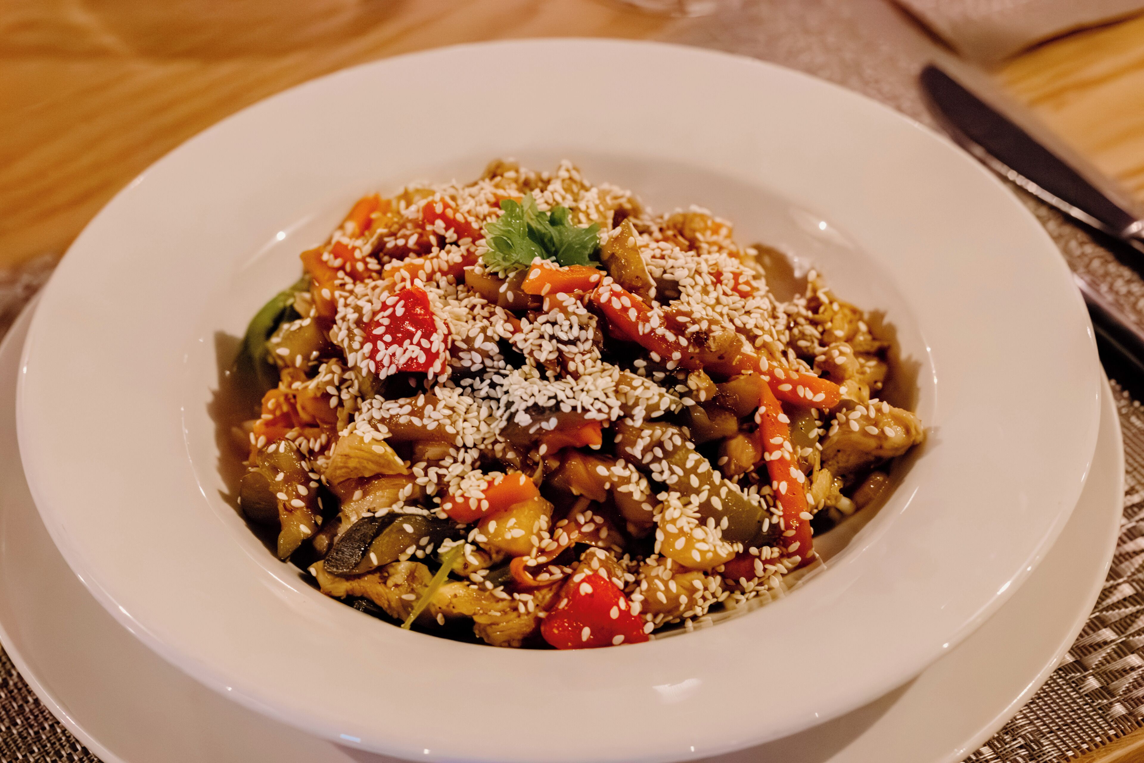 A bowl of stir-fried vegetables and meat garnished with sesame seeds and a sprig of parsley.