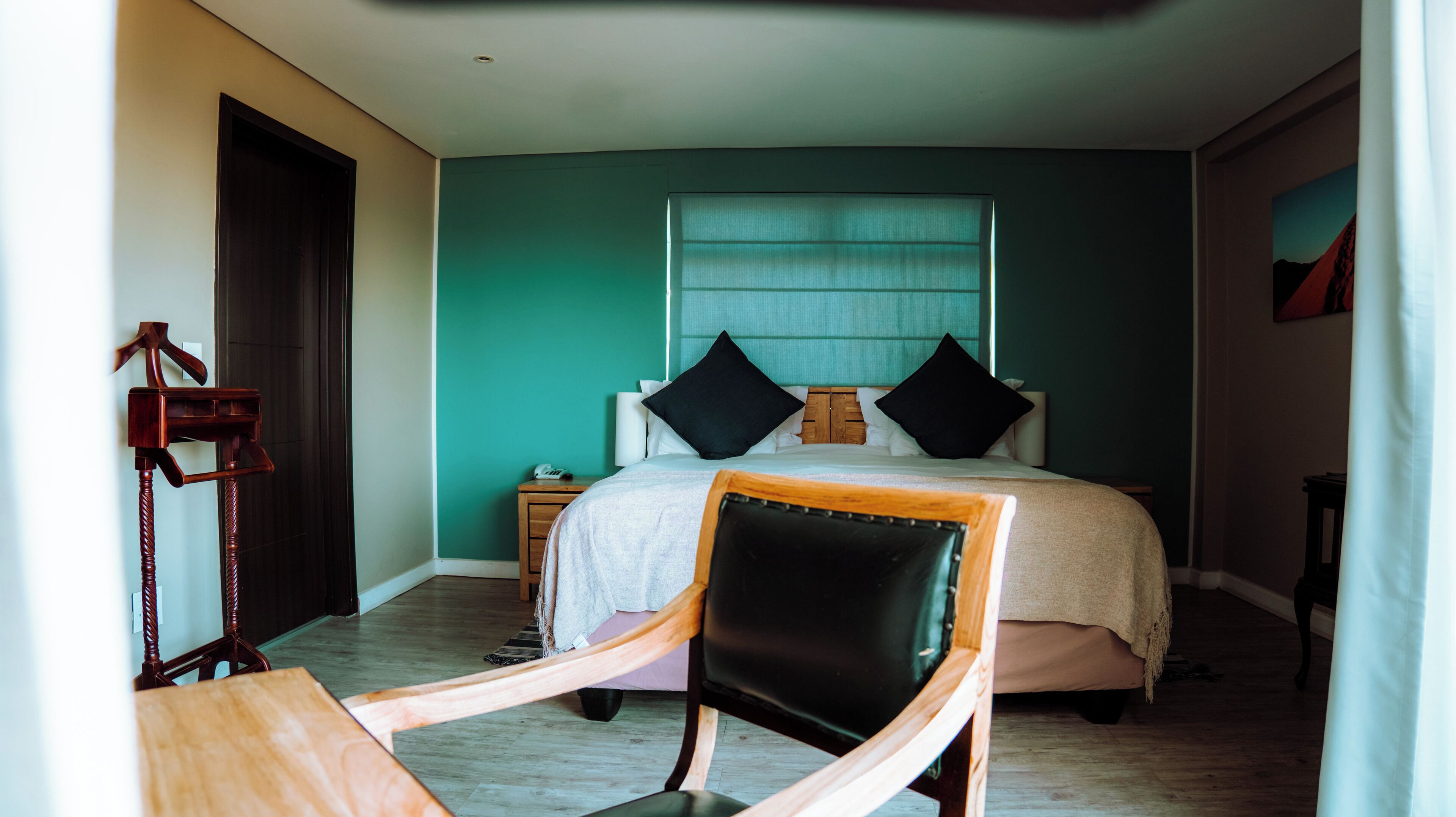 Ein Schlafzimmer mit einem Bett, einem Holzsessel, einem Nachttisch und einer Wandleuchte.
