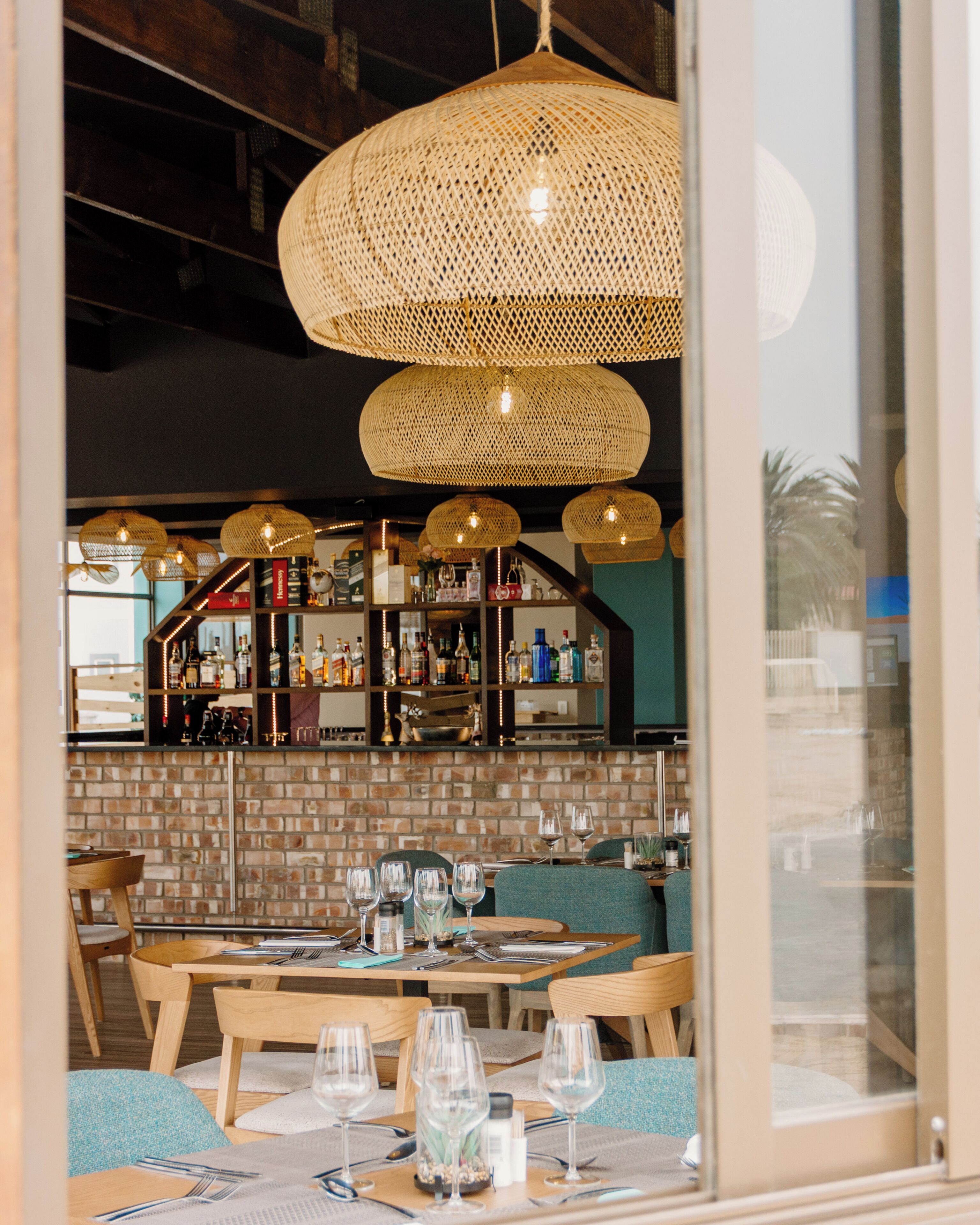 L’intérieur d’un restaurant, avec des lampes en osier au plafond, un mur en briques et un bar à l’arrière-plan.