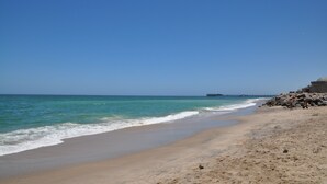 Una platja amb cel blau, aigua tranquil·la i un moll a la distància.