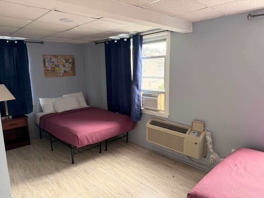 Ein Schlafzimmer mit einem Bett, einem Heizkörper, einem Fenster mit Vorhängen und einer Wandklimaanlage.