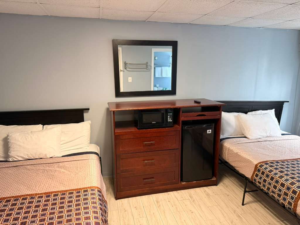A hotel room with two beds, a wooden dresser with a microwave, a small refrigerator, and a mirror on the wall.