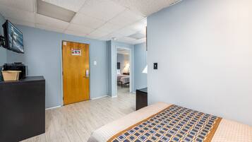 A hotel room with a bed, a desk, a dresser, and a door leading to another room.