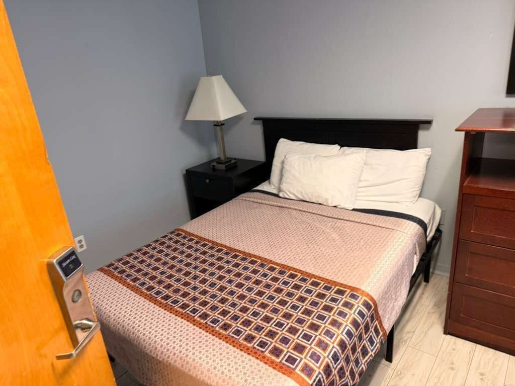 Una habitación de hotel con una cama, una mesita de noche, una lámpara y un aparador de madera.
