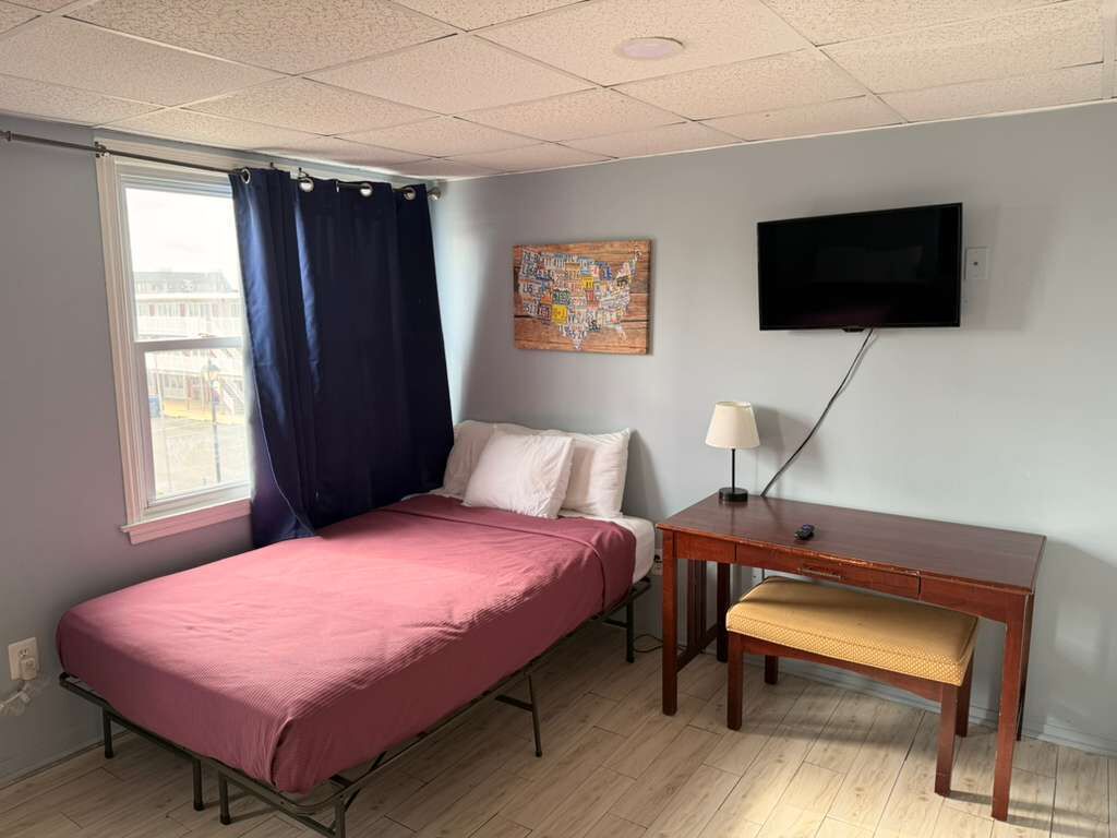 A room with a bed, a desk, a chair, a television, and a window with curtains.