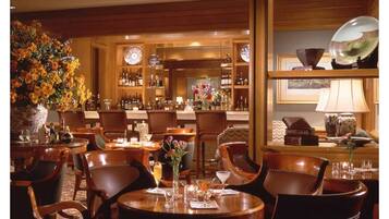 Un elegante bar bien iluminado con mobiliario de madera, un gran arreglo floral y una variedad de botellas y copas en estantes.