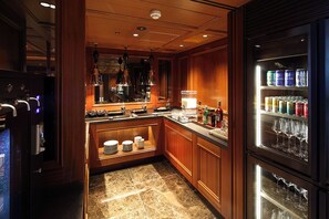 A well-lit bar area with a marble countertop, a wine cooler with glasses, and a variety of beverages.