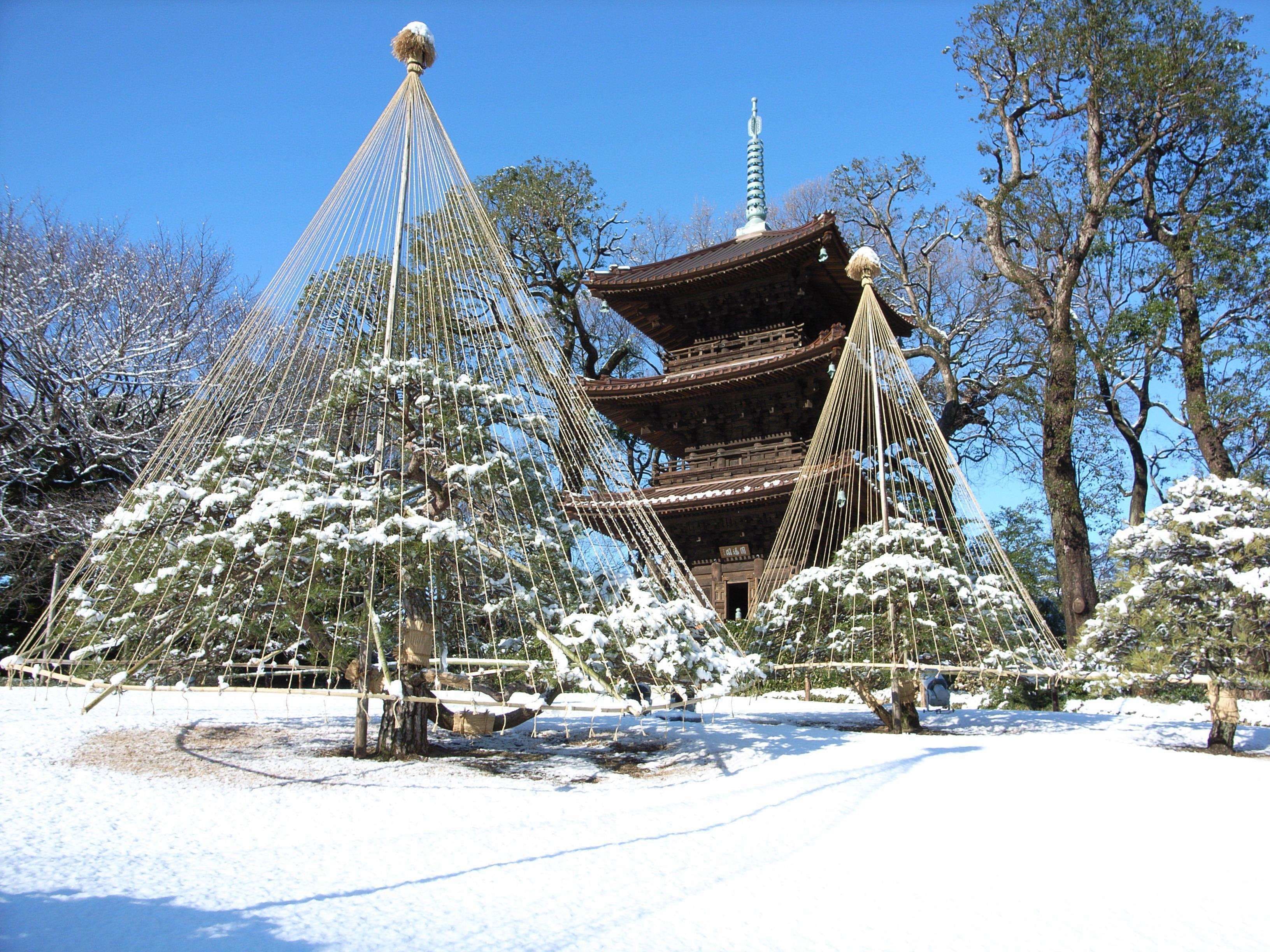 A traditional Japanese pagoda with a snow-covered garden, including a rope bridge and snow-laden trees.