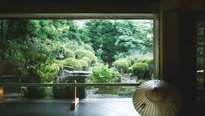 Ein traditioneller japanischer Raum mit Blick auf einen üppigen Garten, einem Holzboden und einem großen Fenster.