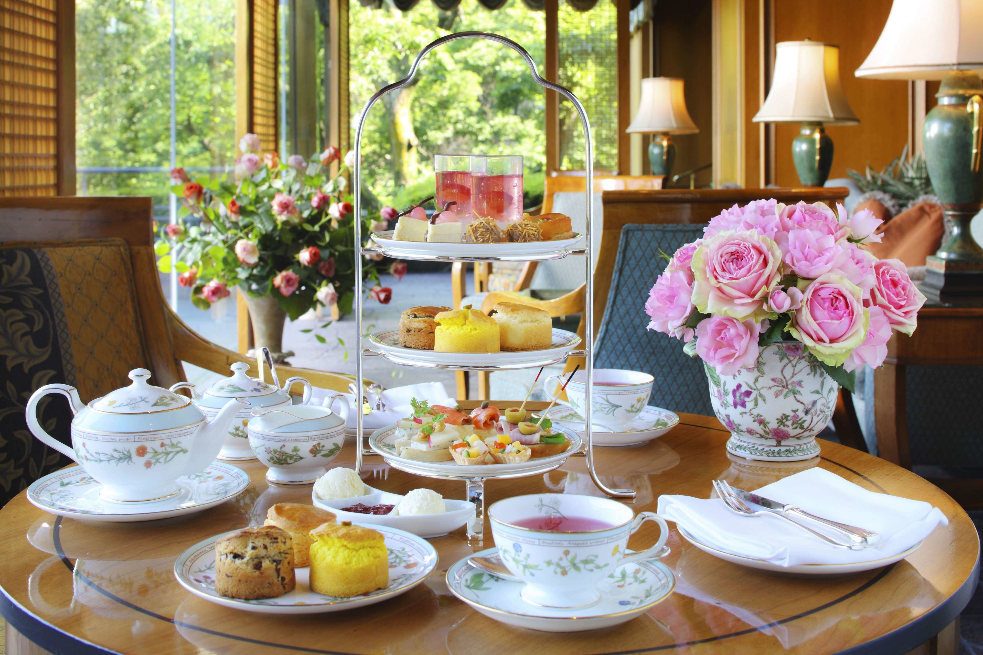 A tea service set on a table with a tiered stand, a vase of flowers, and various pastries and sandwiches.