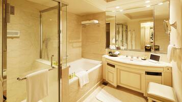 A modern bathroom with a glass-enclosed shower, a large bathtub, a vanity with a mirror, and a small seating area.