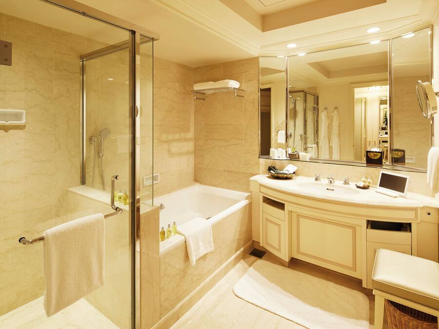 A modern bathroom with a glass-enclosed shower, a large bathtub, a vanity with a mirror, and a small seating area.