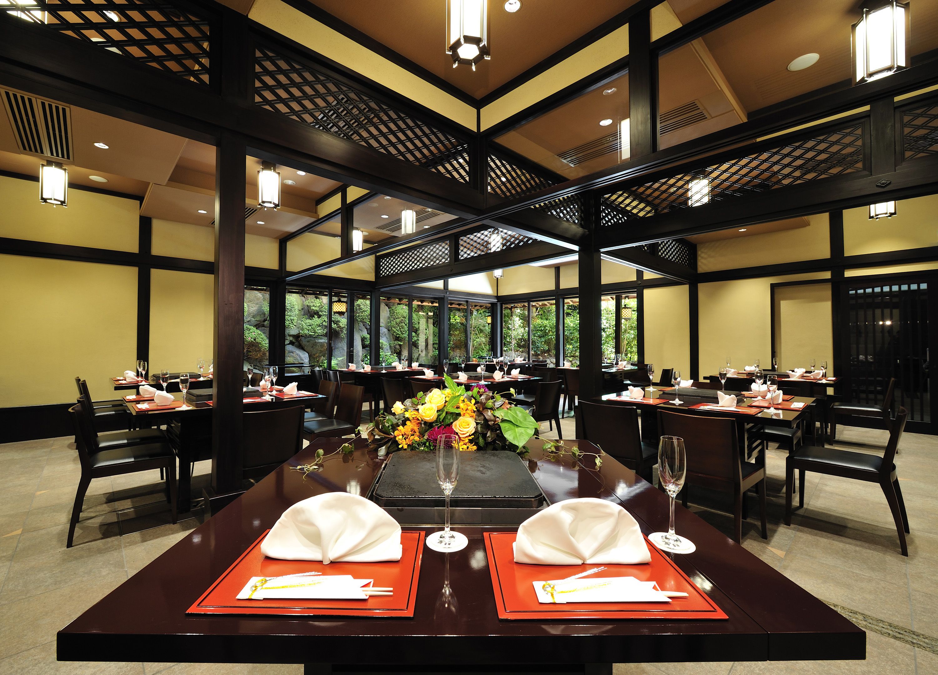 A restaurant with tables set for dining, featuring a central floral arrangement and a view of greenery outside.