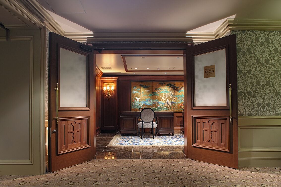 A hotel lobby with a traditional design, featuring a reception desk, a chair, and a decorative wall.