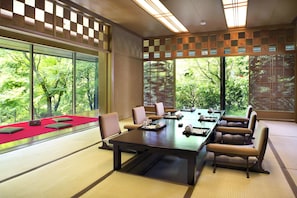 A conference room with a large table, chairs, and large windows offering a view of trees.